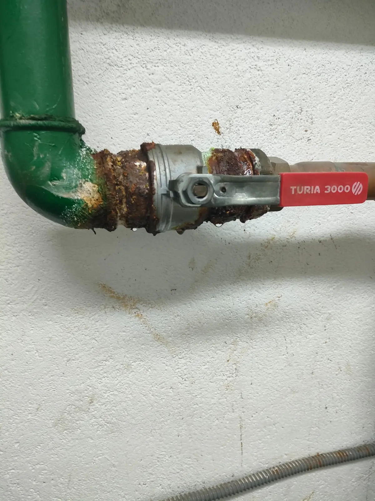 Llave de paso de bola en una tubería verde con uniones muy oxidadas