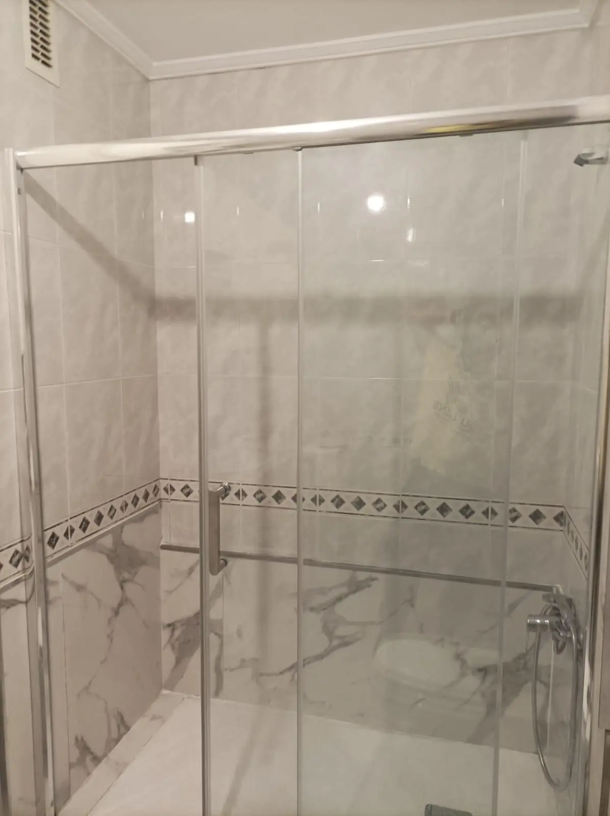 Mampara de ducha de cristal con barra y grifería en paredes de azulejo y mármol